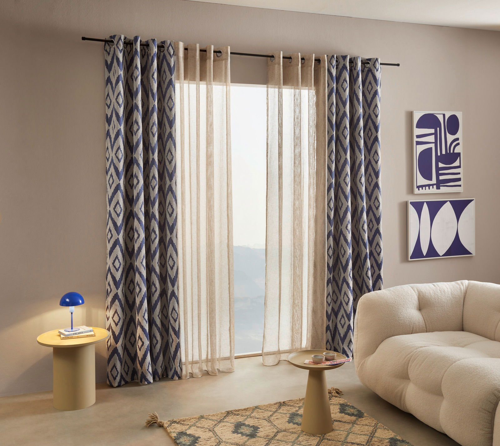 Dieter Knoll ÖSENSCHAL 140x245cm Ösenschal mit blau-weißem geometrischem Muster, aufgehängt vor einem Fenster in einem modernen Wohnzimmer. Perspektive von schräg vorne.