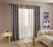 Ösenschal mit blau-weißem geometrischem Muster, aufgehängt vor einem Fenster in einem modernen Wohnzimmer. Perspektive von schräg vorne.