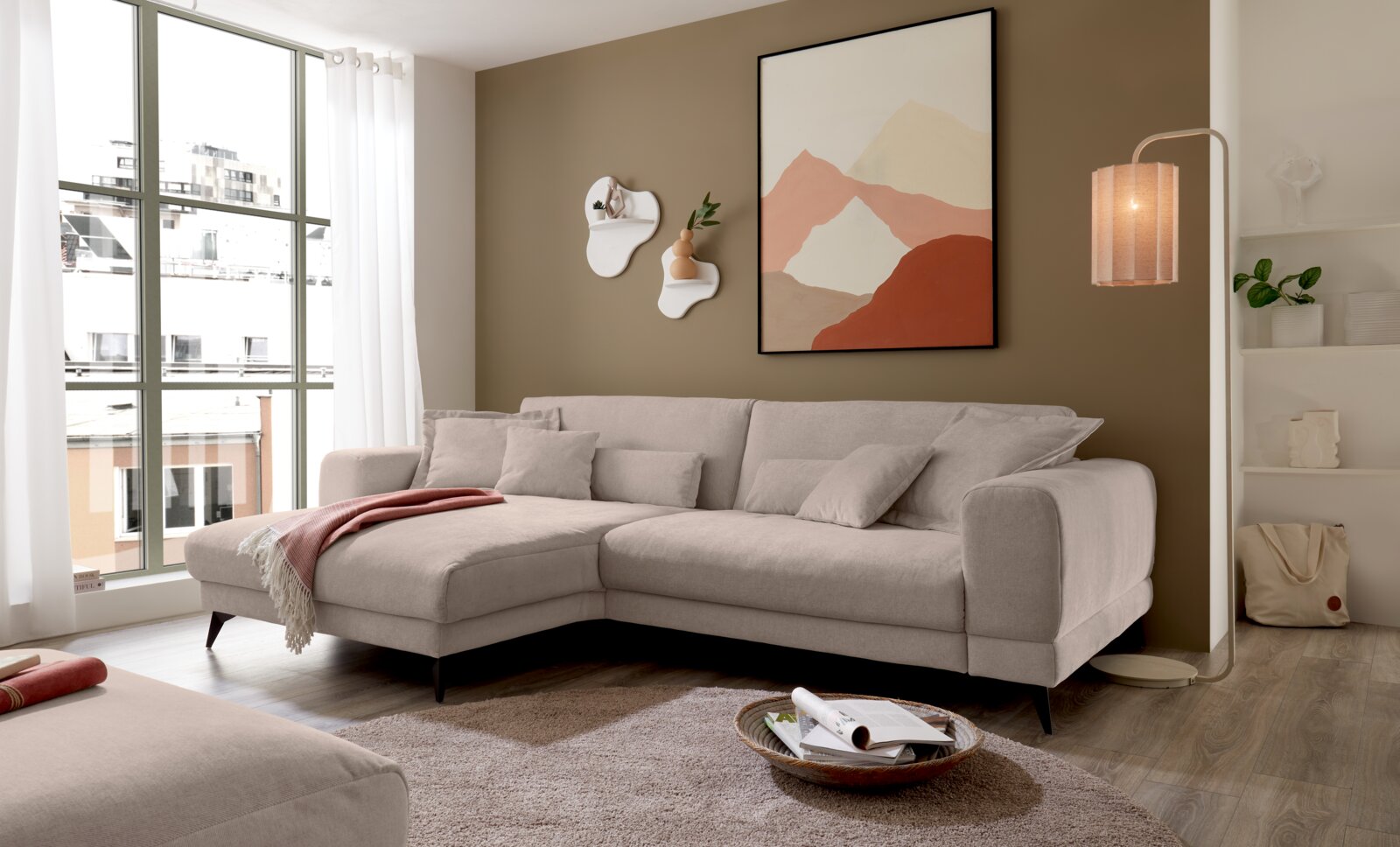 Set one by Musterring Ecksofa SET ONE MIDLAND Modernes hellbeiges L-förmiges Ecksofa mit Recamiere links und mehreren Kissen im Wohnzimmer, fotografiert in leichter Schrägansicht von vorne.