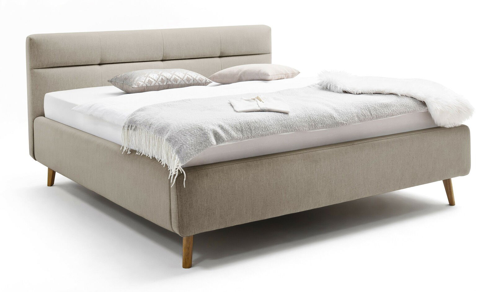 Beiges Polsterbett mit Kopfteil, seitlicher Blickwinkel, dekoriert mit Kissen und Decke.