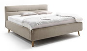 Beiges Polsterbett mit Kopfteil, seitlicher Blickwinkel, dekoriert mit Kissen und Decke.