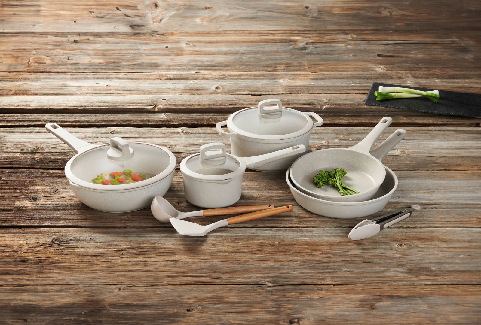 Kochset aus acht Teilen, bestehend aus Töpfen und Pfannen mit Deckeln, auf einer Holzoberfläche von oben fotografiert.