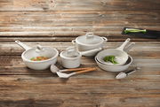 Kochset aus acht Teilen, bestehend aus Töpfen und Pfannen mit Deckeln, auf einer Holzoberfläche von oben fotografiert.