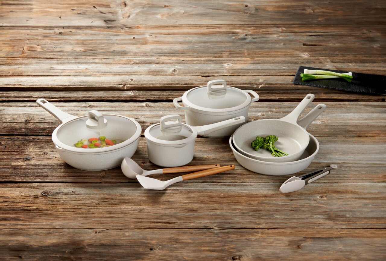 Kochset aus acht Teilen, bestehend aus Töpfen und Pfannen mit Deckeln, auf einer Holzoberfläche von oben fotografiert.