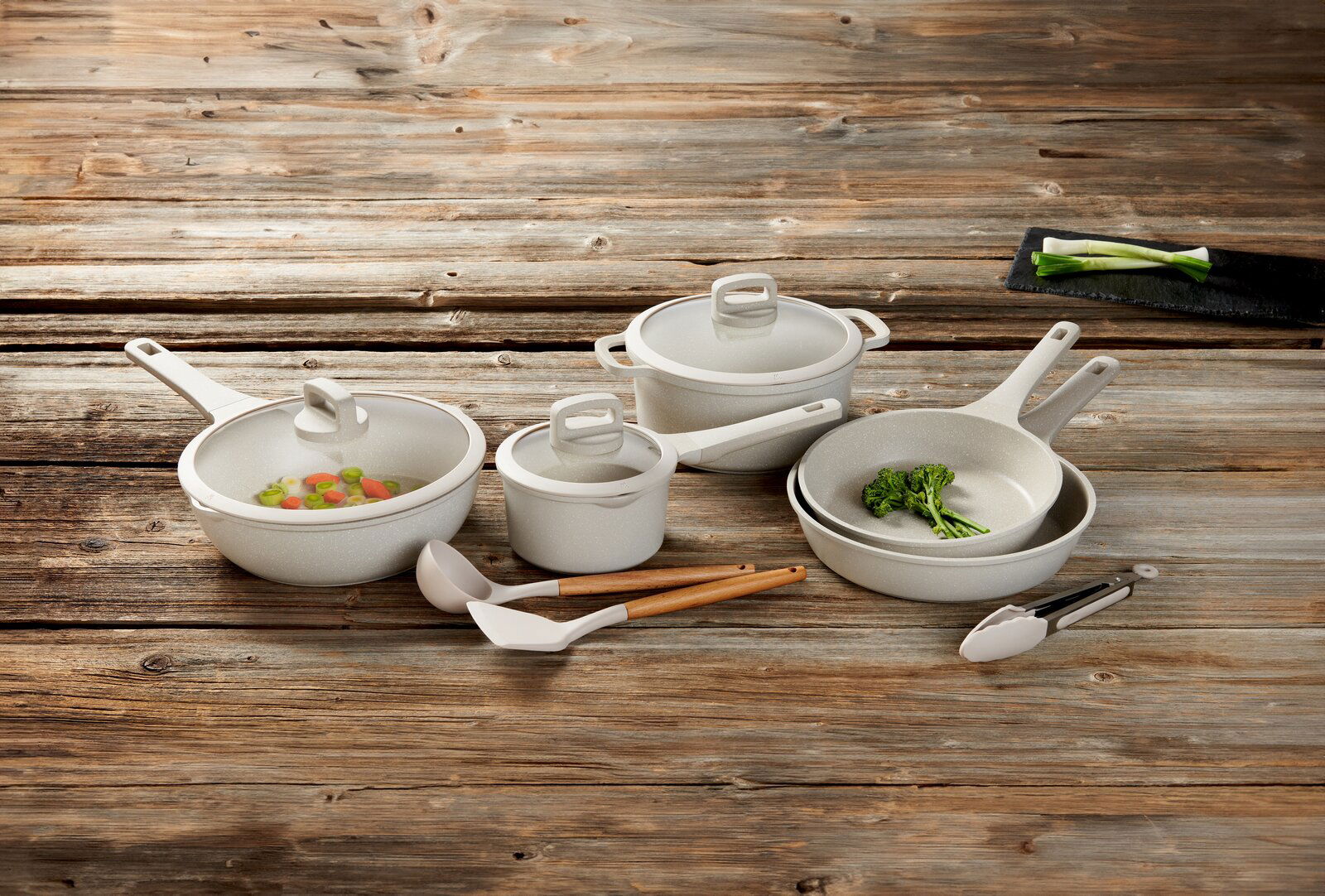 Kochset aus acht Teilen, bestehend aus Töpfen und Pfannen mit Deckeln, auf einer Holzoberfläche von oben fotografiert.