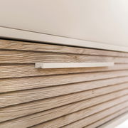 Nahaufnahme einer Kommode mit horizontalen Holzmaserungen und einem modernen, schlichten Griff.