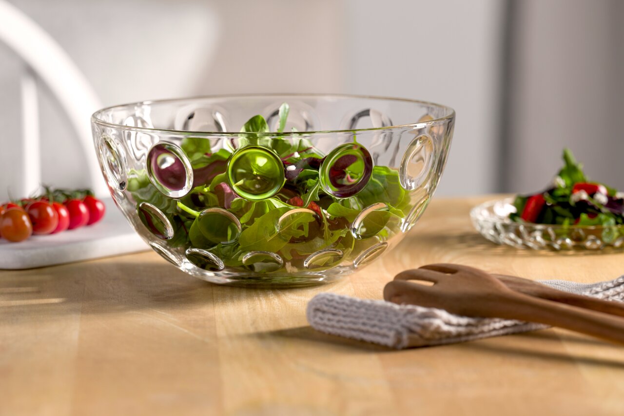 Glas-Schale mit optischem Muster, gefüllt mit frischem Salat, auf einem Holztisch von der Seite fotografiert.