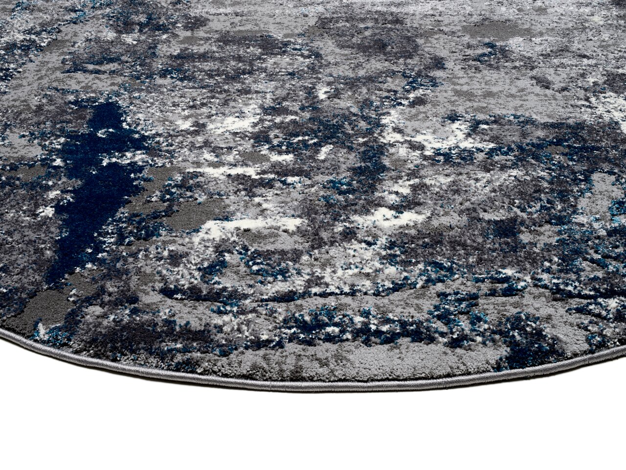 Nahaufnahme eines Designer-Teppichs mit abstraktem Muster in Grau- und Blautönen, perspektivisch von der Seite aufgenommen.