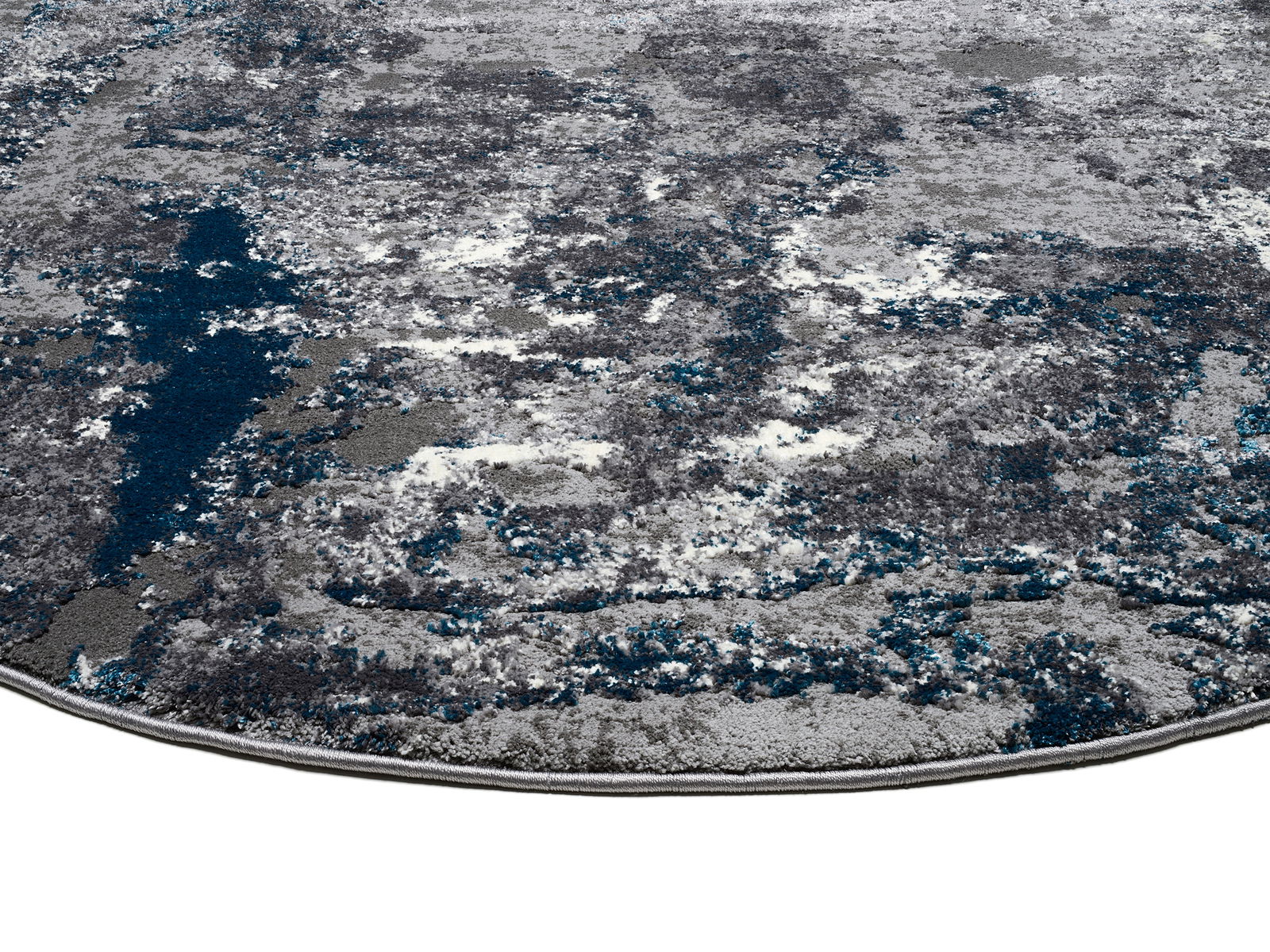 Nahaufnahme eines Designer-Teppichs mit abstraktem Muster in Grau- und Blautönen, perspektivisch von der Seite aufgenommen.
