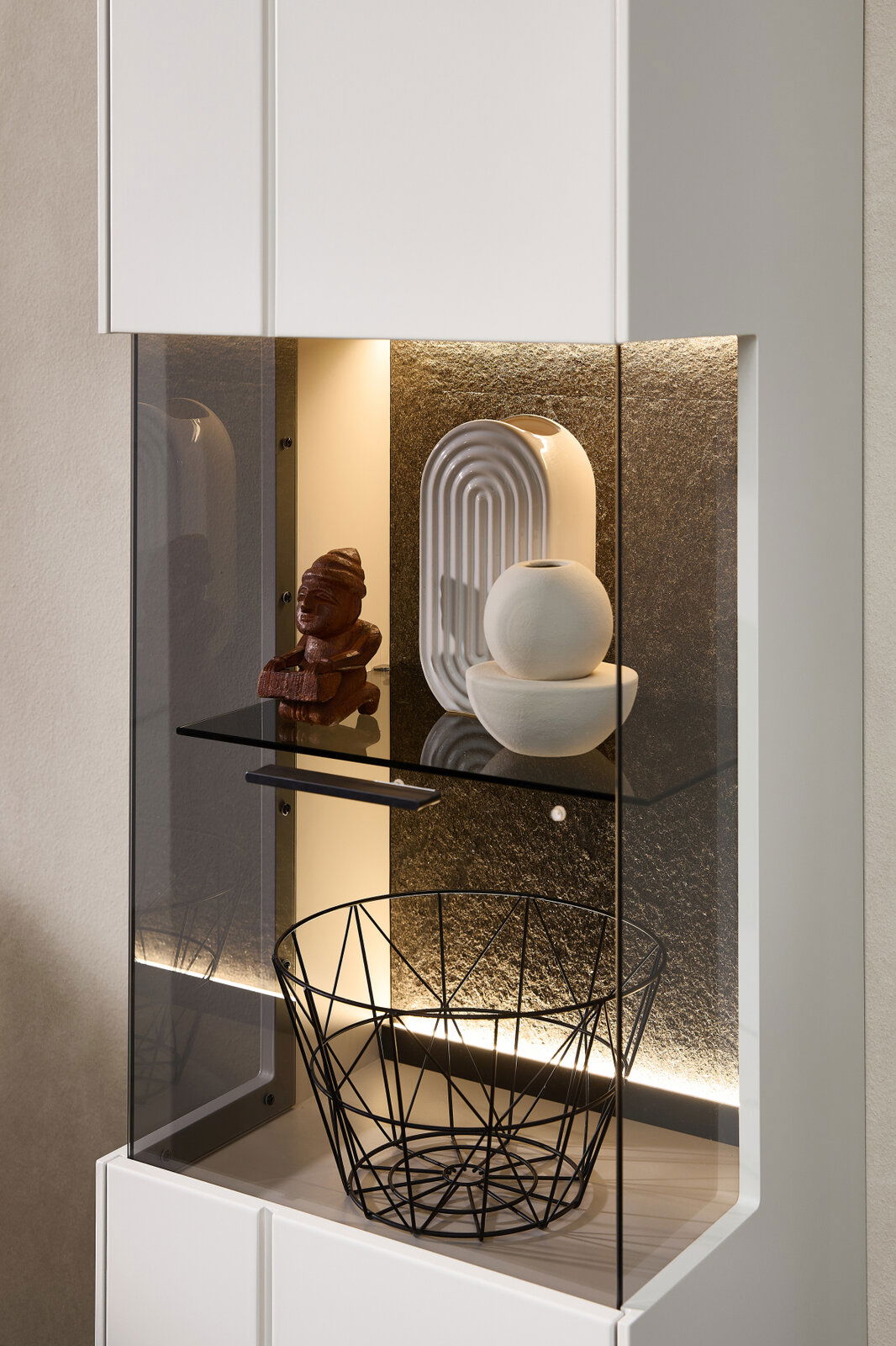 Detailansicht einer modernen Vitrine mit LED-Beleuchtung, dekoriert mit Skulpturen und einem Drahtkorb.