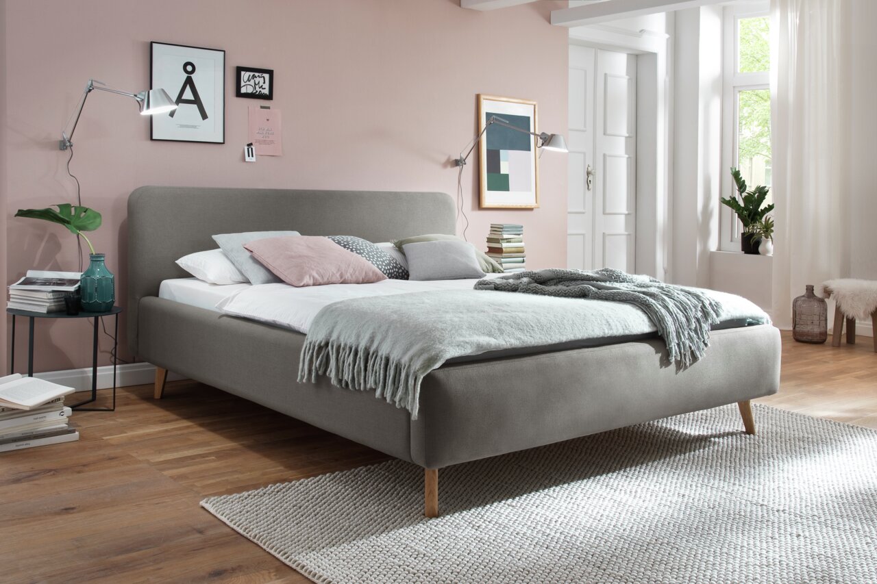 Modernes Polsterbett in Grau mit Holzfüßen, seitliche Perspektive, dekoriert mit Kissen und Decke in einem stilvollen Schlafzimmer.