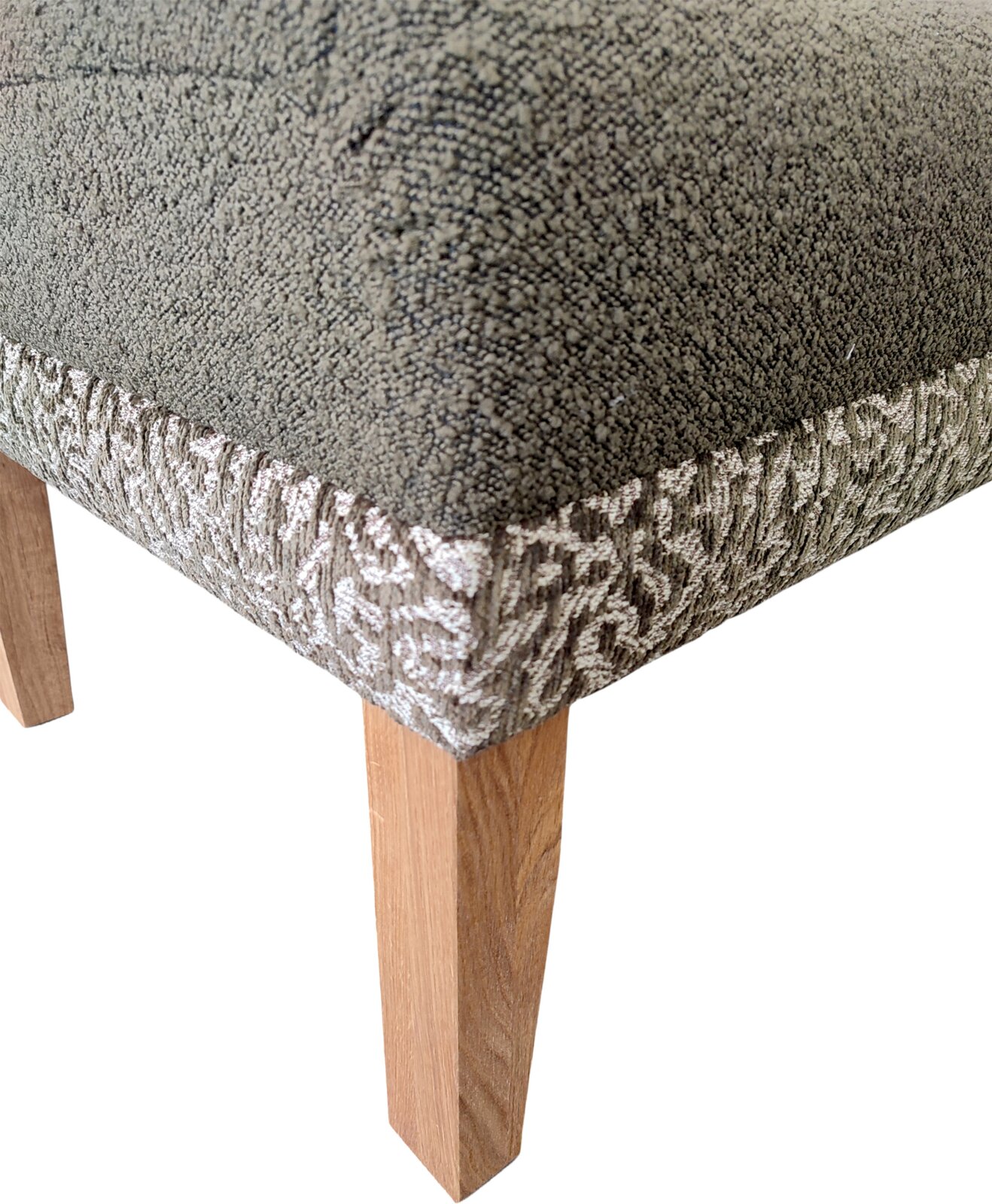 Close-up van de voorste hoek van een gestoffeerde stoel met grijze bekleding, een zijstuk met patroon en een houten poot, schuin van bovenaf gefotografeerd