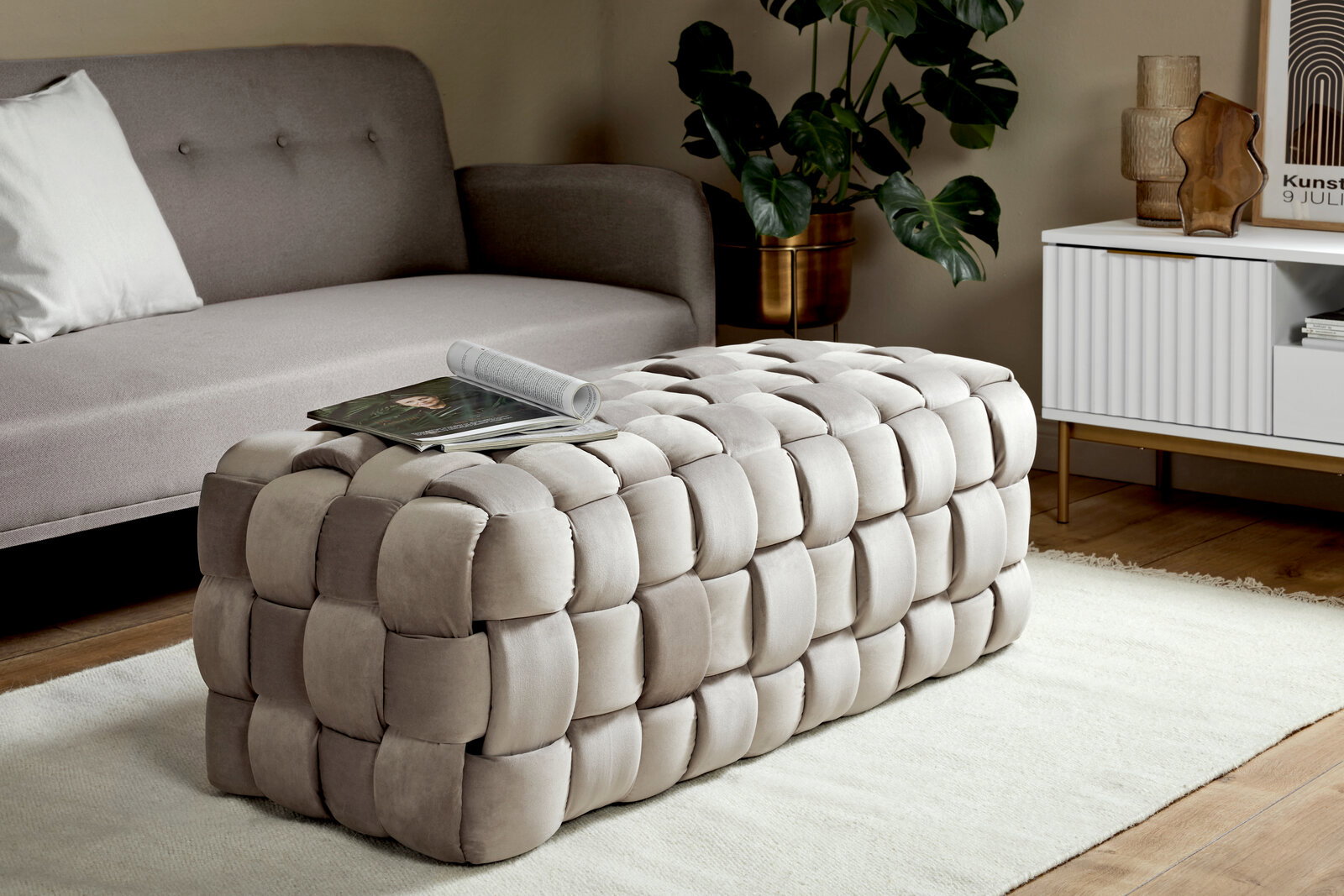 Jahnke Hocker WEB ART Beiger, gepolsterter Hocker in geflochtener Optik, seitliche Perspektive, platziert in einem modernen Wohnzimmer mit Sofa und Beistelltisch.