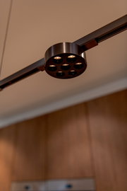 Ronde LED-spot in matzwart met meerdere lenzen op een railverlichting, gezien van onderen in een interieur met warme verlichting