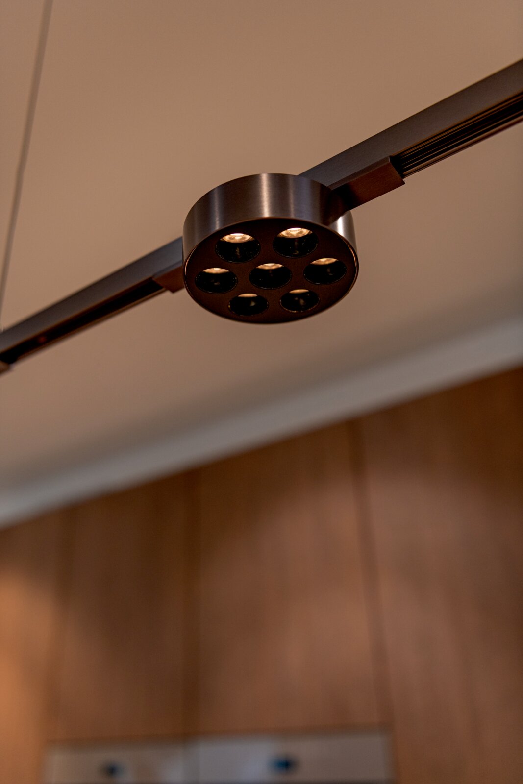 Ronde LED-spot in matzwart met meerdere lenzen op een railverlichting, gezien van onderen in een interieur met warme verlichting