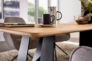 Close-up vanuit een licht zijdelings perspectief: moderne eettafel met een lichtgekleurd houten blad en zwarte metalen poten, met daarop een kopje en een roestvrijstalen kan in de woon-/eetkamer