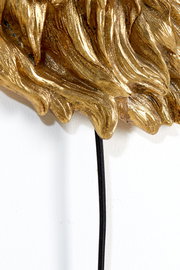 Nahaufnahme einer goldenen Wandleuchte mit detaillierten Verzierungen und einem schwarzen Kabel, von der Seite betrachtet.