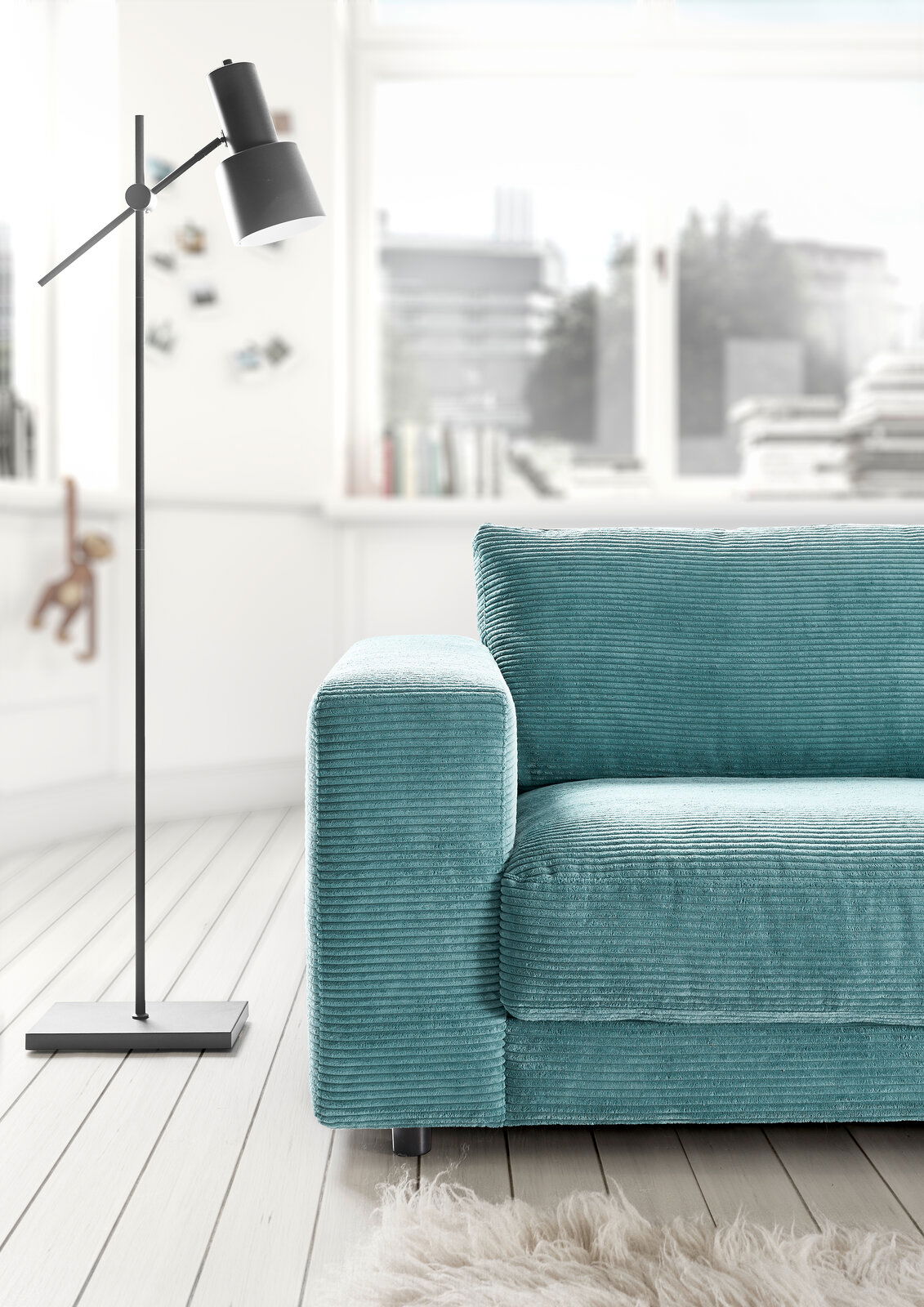 Nahaufnahme eines türkisfarbenen 2-Sitzer-Sofas mit geripptem Stoffbezug, neben einer modernen Stehlampe, in einem hellen Raum mit Holzboden.