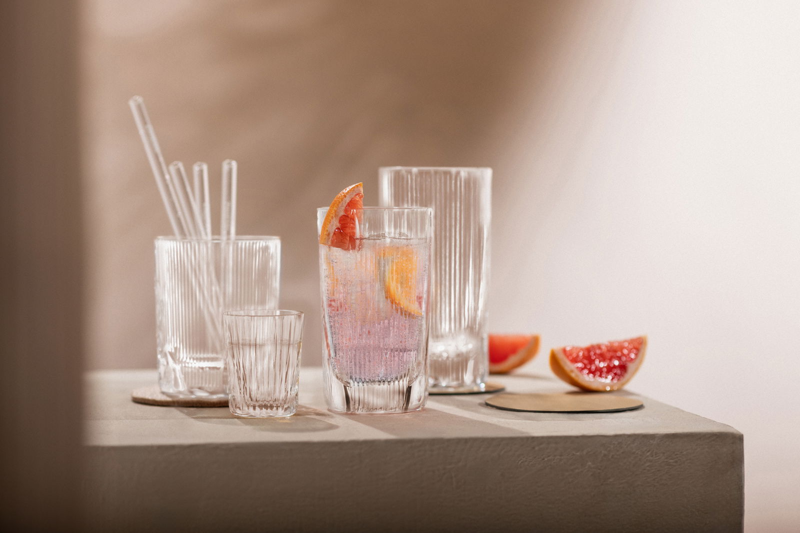 Vier elegante Gläser mit geriffeltem Design, gefüllt mit Getränken und dekoriert mit Grapefruitscheiben, auf einem Tisch aus seitlicher Perspektive.