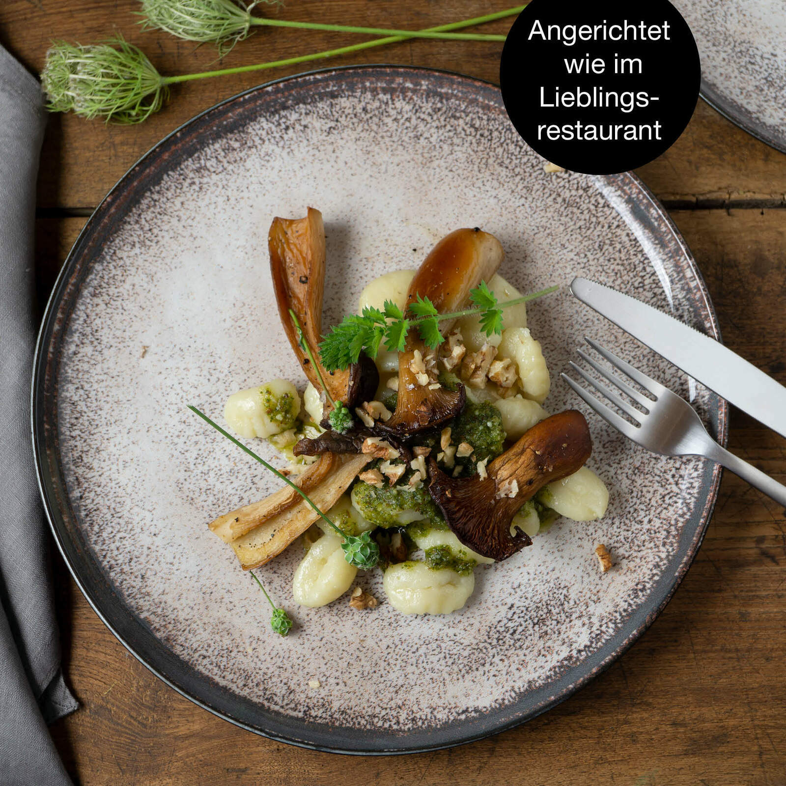 Vogelperspektive auf einen gedeckten Teller mit Gnocchi, Pilzen und Kräutern, angerichtet auf einem beige gesprenkelten Teller.