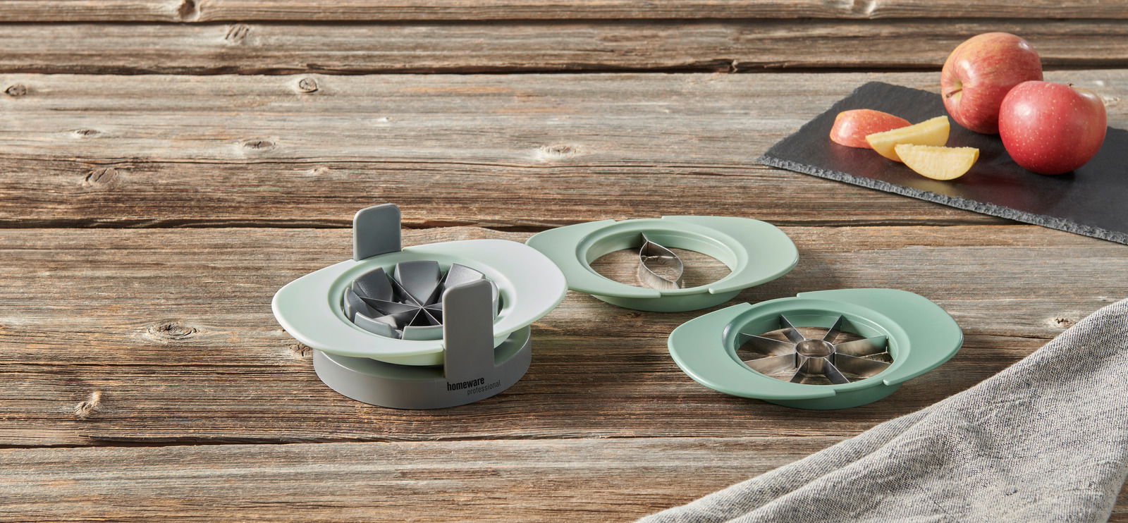 Apfelteiler in drei Teilen auf einem Holztisch, mit Äpfeln im Hintergrund, aus der Vogelperspektive fotografiert.