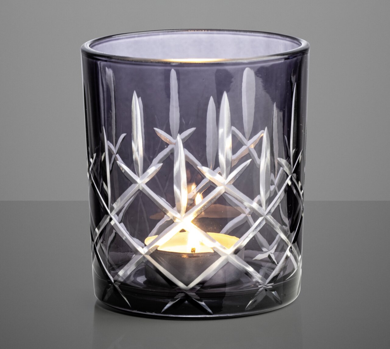 Graues Windlicht mit Schliffmuster, frontal fotografiert, mit brennendem Teelicht im Inneren.