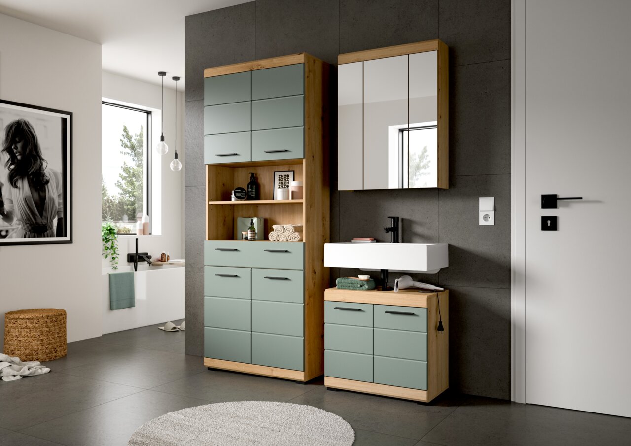 Modernes Badezimmermöbel-Set in Holzoptik mit salbeigrünen Fronten: hoher Hochschrank mit offenen Regalfächern, Waschtischunterschrank mit weißem Aufsatzwaschbecken und Spiegelschrank; Ansicht in leichter Schrägperspektive von vorn.