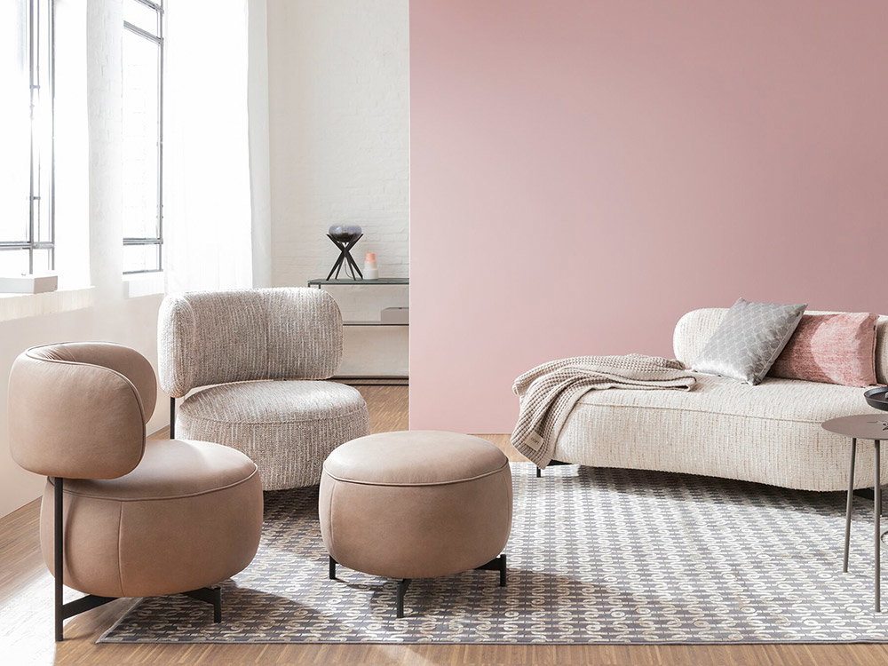 Helles Wohnzimmer mit modernem Sofa, Sessel, Hocker und rosafarbener Wand