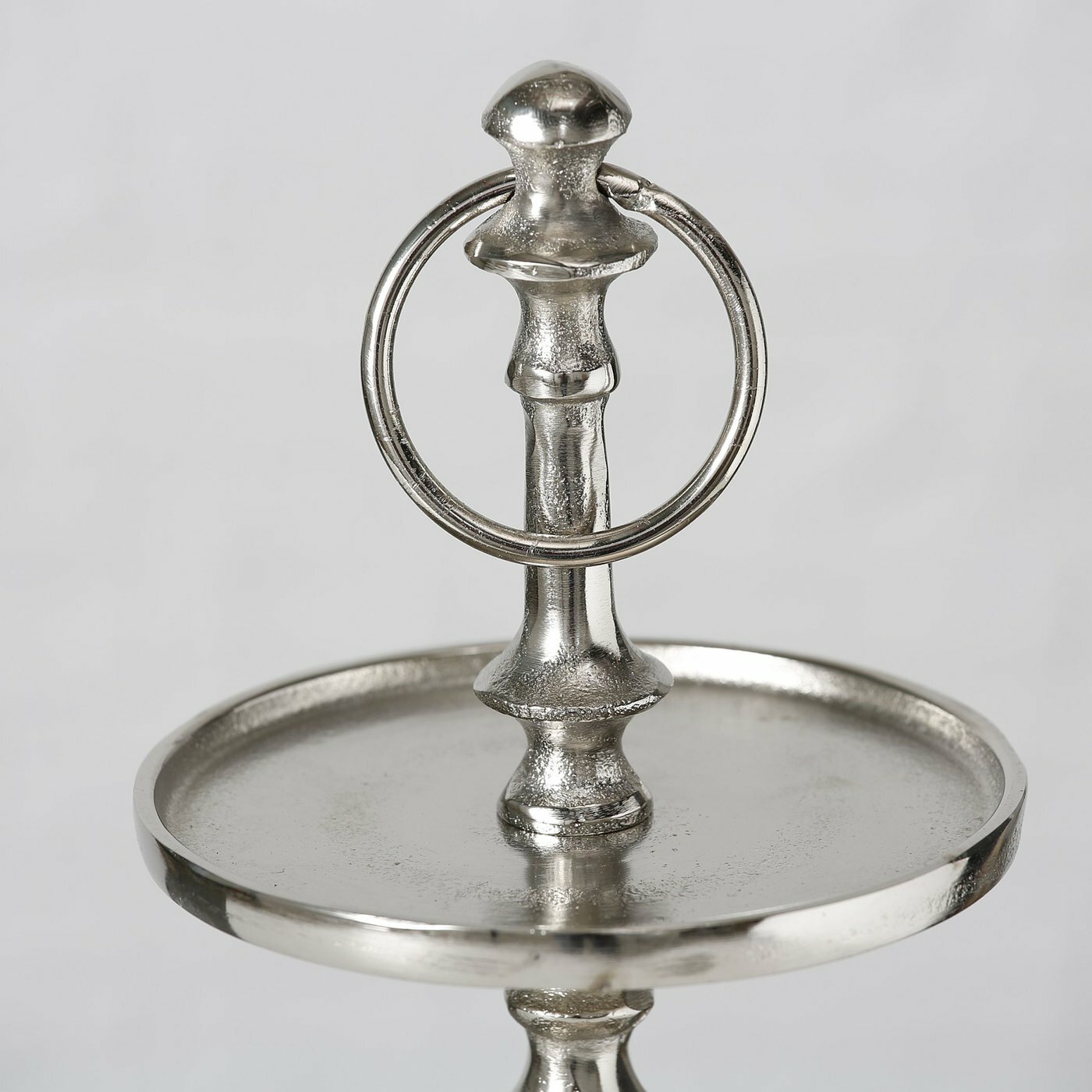 Nahaufnahme einer silbernen Deko-Etagere mit drei Ebenen, elegantes Design mit rundem Griff oben, seitliche Perspektive.