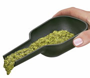 Hand hält einen Gusseisen-Gewürzmörser mit Stößel, gefüllt mit grünem Gewürzbrei, aus seitlicher Perspektive.