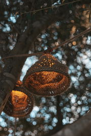 Nahaufnahme einer Outdoor-Lichterkette mit solarbetriebenen, geflochtenen Lampenschirmen, die an einem Baum hängen und warmes Licht ausstrahlen.