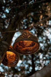 Nahaufnahme einer Outdoor-Lichterkette mit solarbetriebenen, geflochtenen Lampenschirmen, die an einem Baum hängen und warmes Licht ausstrahlen.