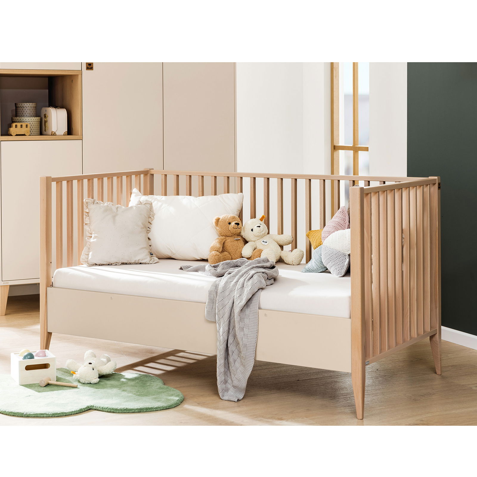 Babybett aus Holz mit Gitterstäben, dekoriert mit Kissen und Kuscheltieren, seitliche Perspektive