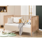 Houten babybedje met spijlen, versierd met kussens en knuffels, zijaanzicht
