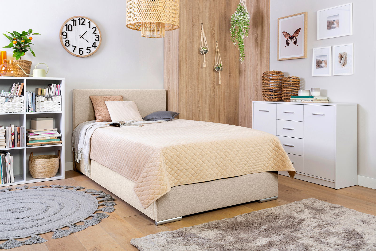Gemütliches Schlafzimmer mit Boxbett 140, beige Bettwäsche, Bücherregal, Wanduhr und Dekorationen, seitliche Perspektive
