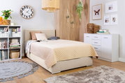 Gezellige slaapkamer met een boxbed van 140 cm, beige beddengoed, boekenkast, wandklok en decoraties, zijaanzicht