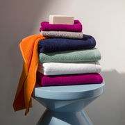 Stapel bunter Handtücher mit Seife auf einem blauen Hocker, seitliche Perspektive