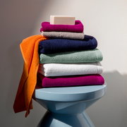 Stapel bunter Handtücher mit Seife auf einem blauen Hocker, seitliche Perspektive