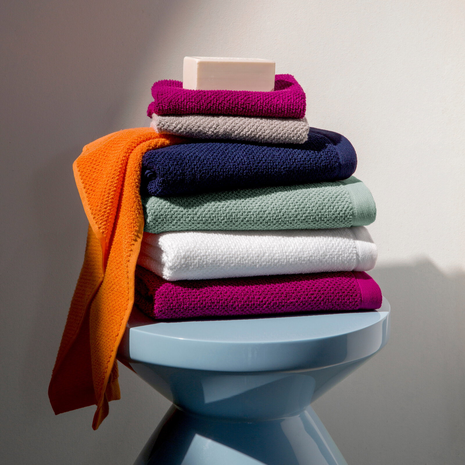 Stapel bunter Handtücher mit Seife auf einem blauen Hocker, seitliche Perspektive
