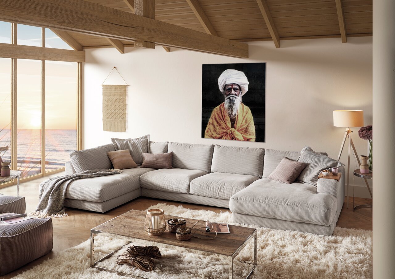 Pure Home Lifestyle Wohnlandschaft PURE 979 Gemütliche Polsterrundecke in einem modernen Wohnzimmer mit Blick auf das Meer durch große Fenster, dekoriert mit Kissen und Decken, aus der Perspektive von vorne links.