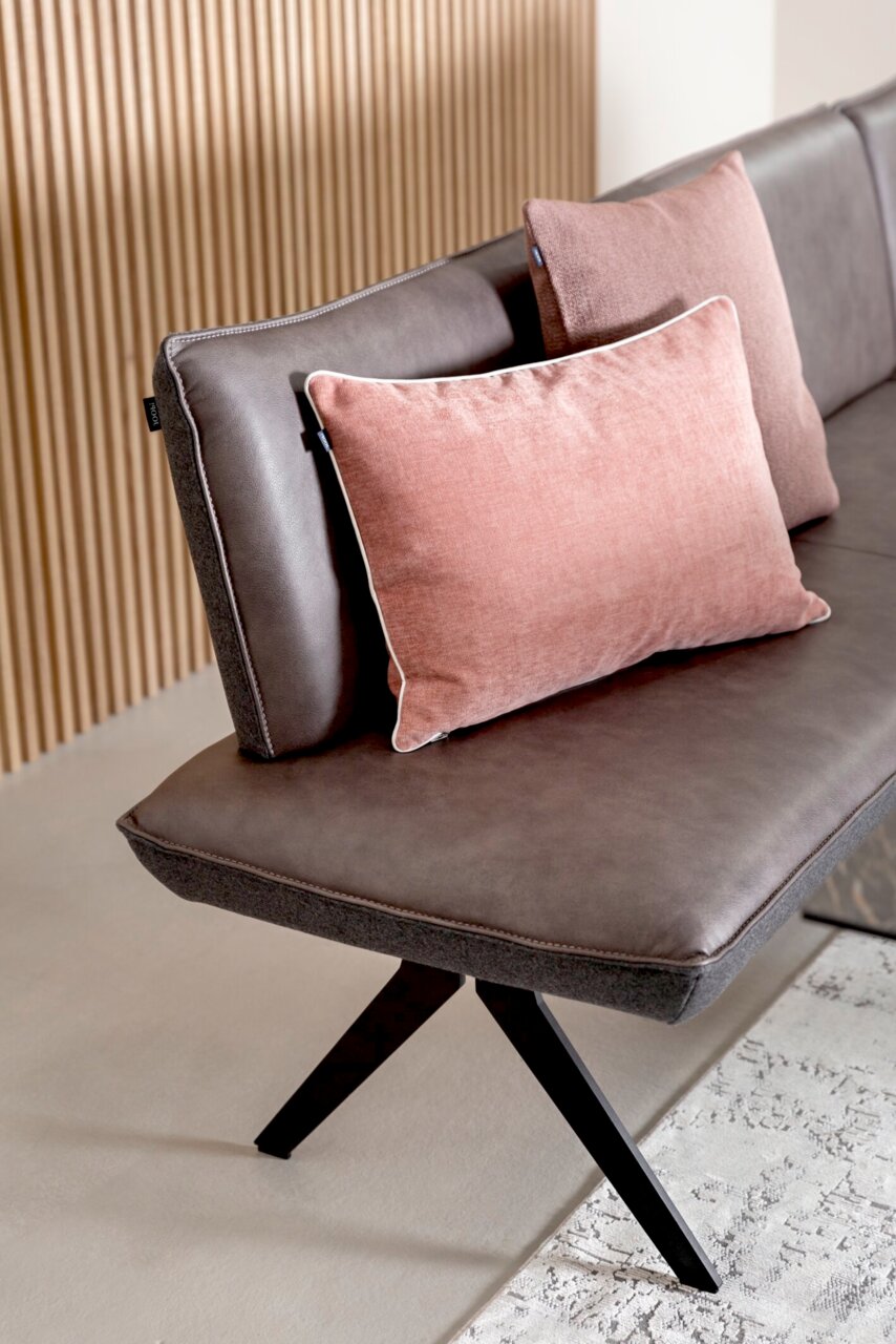 Eckbank in seitlicher Perspektive mit braunem Lederbezug und rosa Kissen, modernes Design mit schwarzen Metallbeinen.