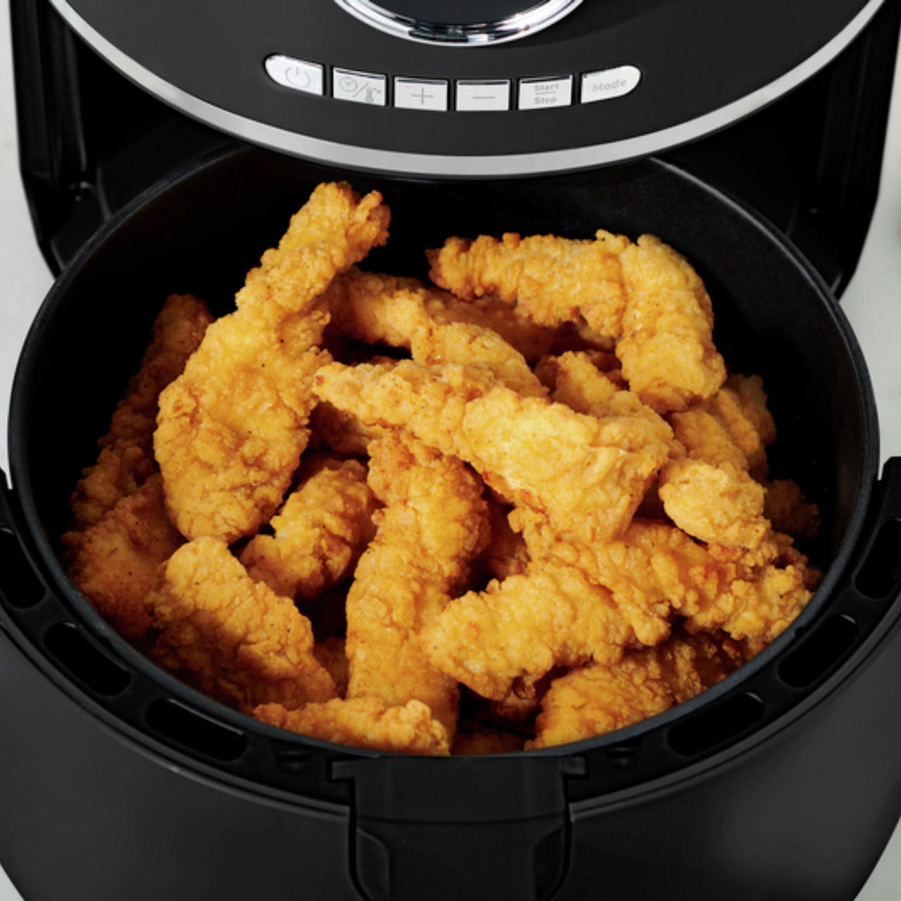 Nahaufnahme einer geöffneten Heißluftfritteuse mit knusprigen, goldbraunen Hähnchenstreifen.