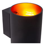 Nahaufnahme einer modernen, zylindrischen Wandleuchte in Schwarz mit leuchtend orangefarbener Innenfläche, die warmes Licht abstrahlt.
