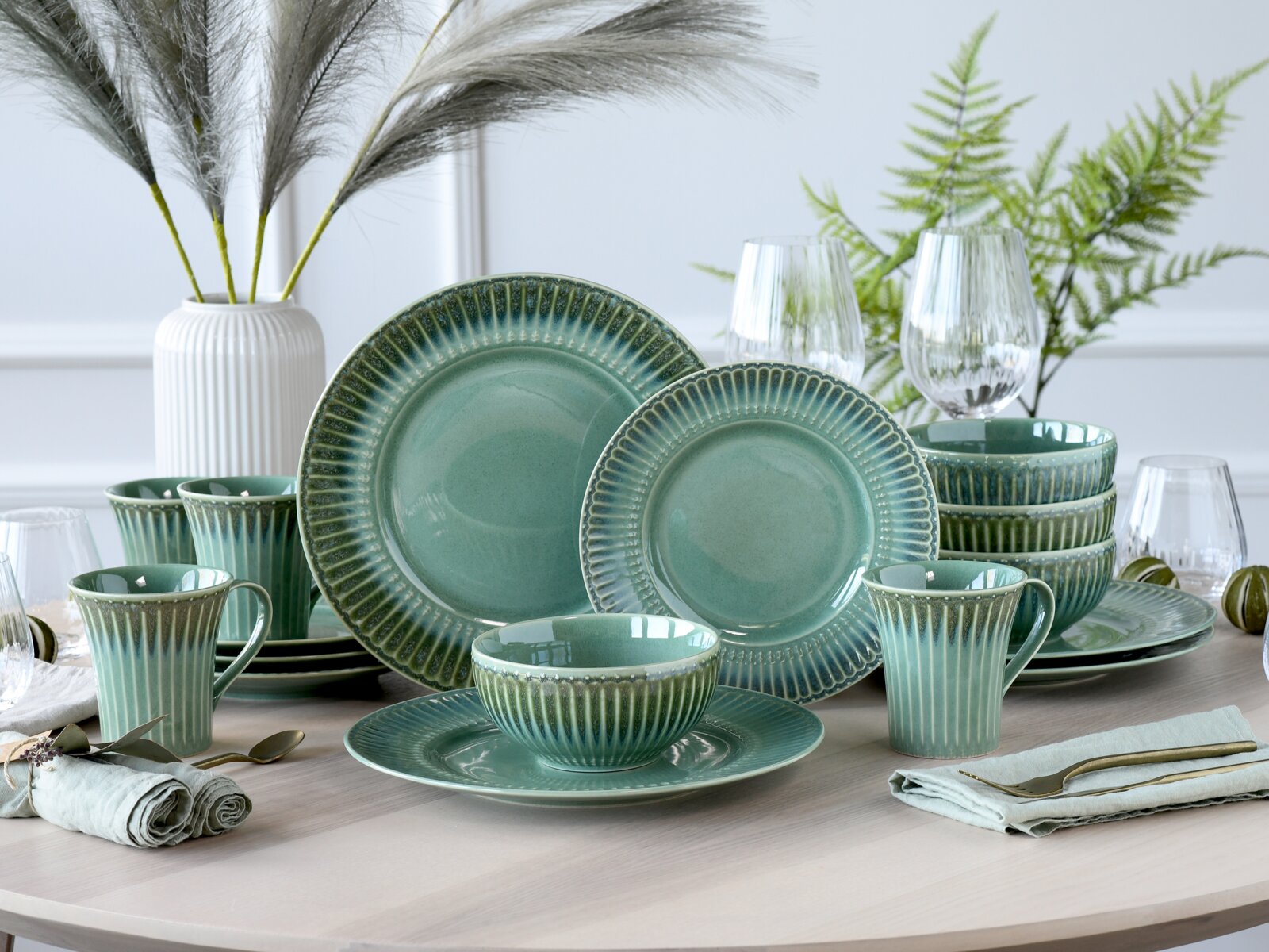 Creatable Kombiservice 16-tlg CELADON Türkis-grünes Keramik-Geschirrset mit gerilltem Rand (Teller, Schalen und Tassen) auf gedecktem Tisch, dekoriert mit Gläsern und Pflanzen, Perspektive: leicht seitliche Frontansicht auf Augenhöhe.