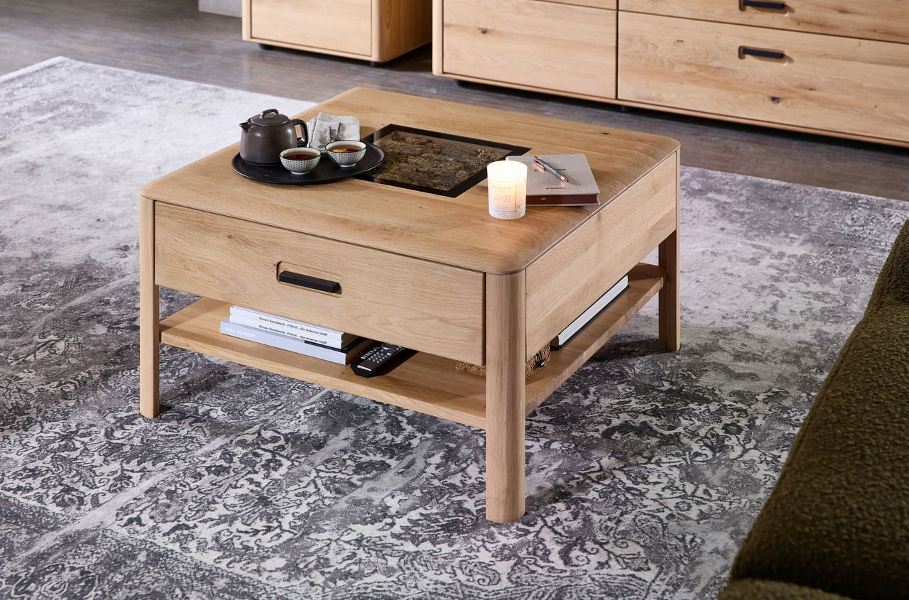 Moderner Couchtisch aus Holz mit Glasplatte und Schublade, von schräg oben fotografiert. Auf dem Tisch stehen eine Teekanne, Tassen und eine Kerze.