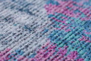 Nahaufnahme eines bunten Teppichs mit einem Muster in Blau-, Rosa- und Grautönen, aus seitlicher Perspektive.