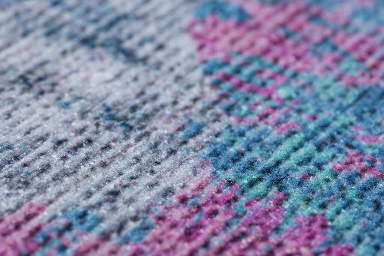 Nahaufnahme eines bunten Teppichs mit einem Muster in Blau-, Rosa- und Grautönen, aus seitlicher Perspektive.