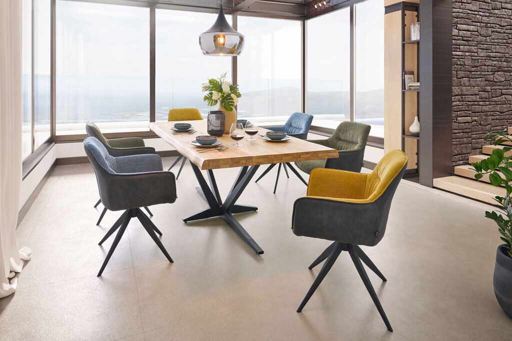 Esszimmer mit modernem Tisch und sechs bunten Sesseln in einem hellen Raum mit Panoramafenstern, seitliche Perspektive.