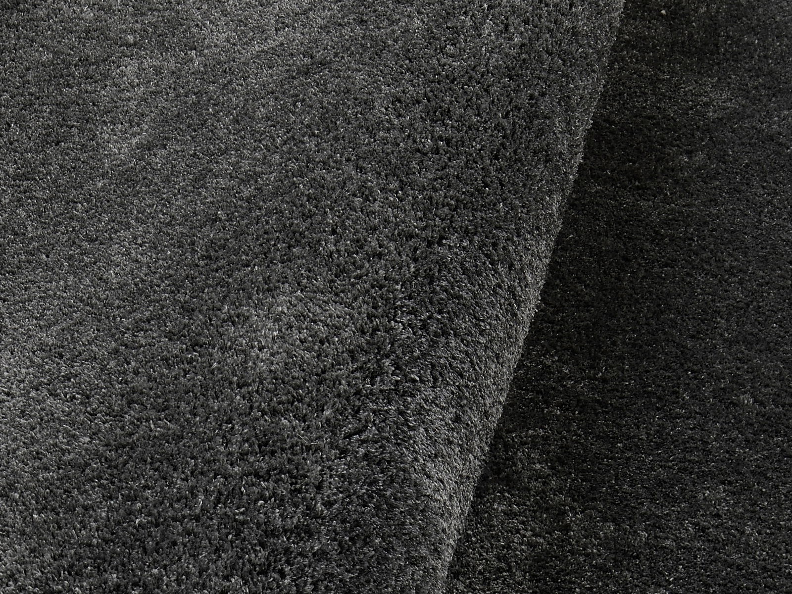Nahaufnahme eines dunkelgrauen Hochflor-Teppichs mit weicher, flauschiger Textur.