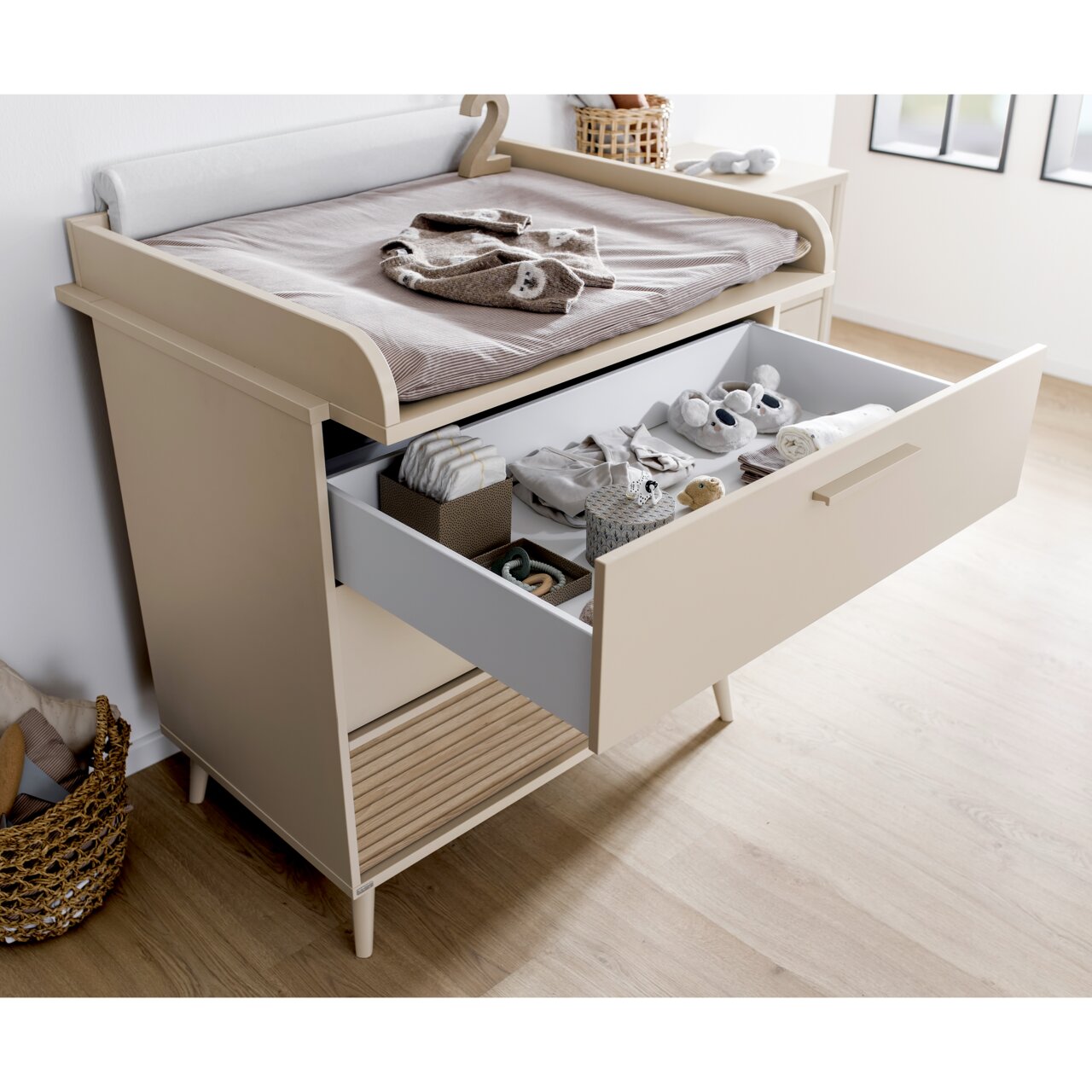 Een smal commode in een moderne kinderkamer, zijaanzicht met geopende lade, gevuld met babyspullen.